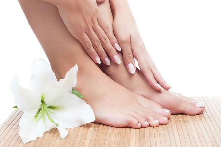 Woman with manicured nails touching feet with a white flower by her foot
